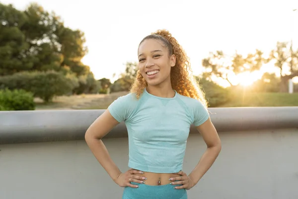 portrait pretty sporty Hispanic woman with blonde curly hair, outdoors at sunset