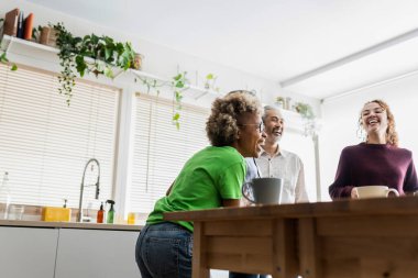 friends in kitchen at home having fun, focus on blonde afro american woman