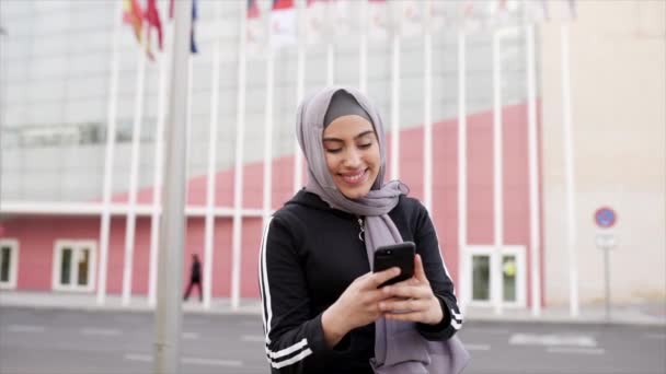 市中心一名戴着头巾的年轻漂亮的穆斯林妇女用手机微笑着看着她 — 图库视频影像