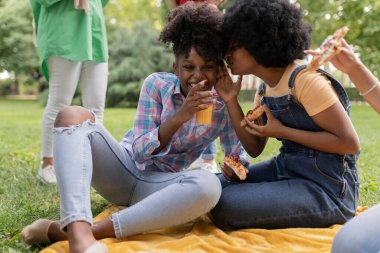 multiracial friends on a picnic in the park, female friends whispering a secret in the ear