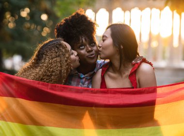 Üç arkadaş gay gurur bayrağıyla öpüşüyor, Igbt gökkuşağı, mutlu kadınlar dışarıda gökkuşağı bayrağı öpüyor ve giyiyorlar - aşk ve lezbiyen günbatımı konsepti - yumuşak odak -