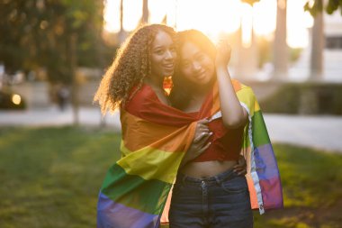 multiracial women with gay pride rainbow flag at sunset