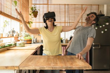 Olgun modern kadın kocasıyla oturma odasında sanal gerçeklik simülatörü kullanıyor.