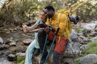 multiracial young couple on mountain with smartphone backpackers