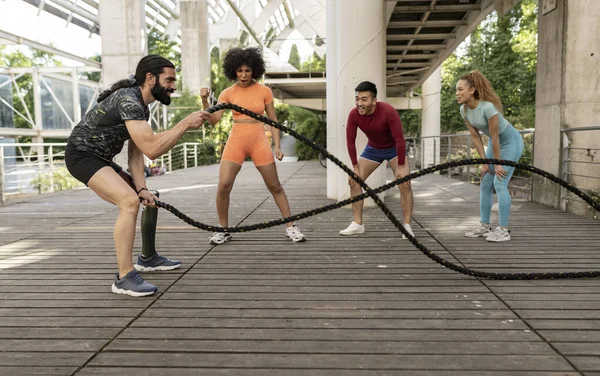 group of multiracial young sports friends doing intense training outdoors - focus on man with leg prosthesis using a rope -