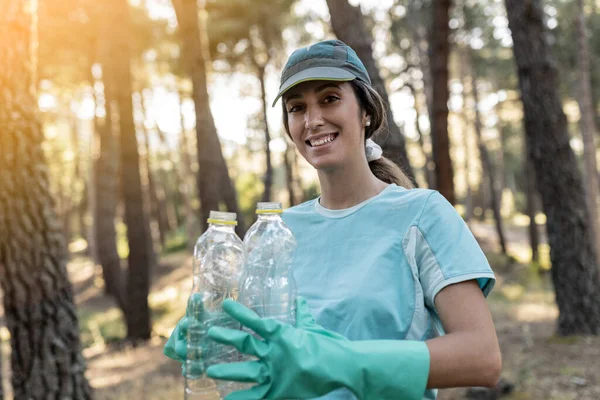 Caucasian woman volunteering to collect garbage in the forest, pretty smiling young woman collecting forest garbage,