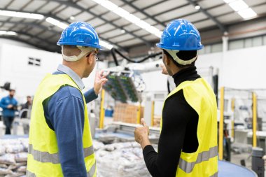 multiracial engineer colleagues checking operation of robotic arm in factory