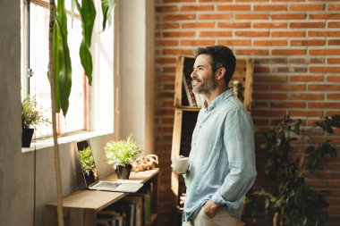 mature man at home looks out the window while having a glass of coffee for breakfast