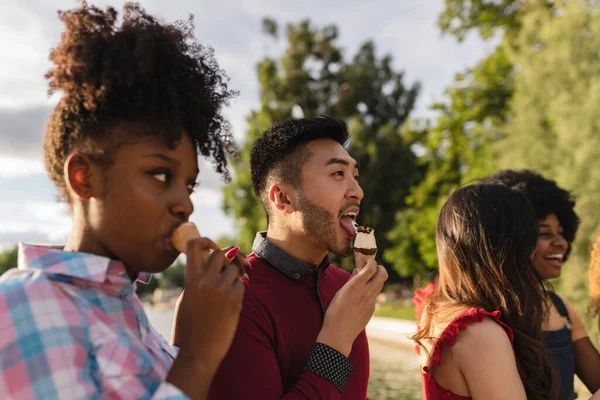 multiracial adult friends eat ice cream in the park in summer - focus on asian man -