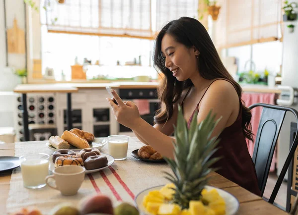 asian woman have breakfast at home while looking at her smartphone