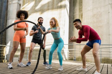 Fitness multiracial people exercising with battle ropes at the gym. Hispanic woman using the ropes training alongside her peers who cheer her on, arms and cardio.