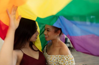 İki çok ırklı kadın, gökkuşağına sarılmış eşcinsel gurur bayrağı