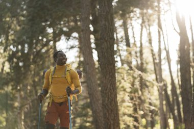 Günbatımında ormanda mutlu bir Afrikalı Amerikalı adam Sırt çantalı bir yürüyüşçü açık havada başarıyı kutluyor insanlar, başarı ve spor kavramı