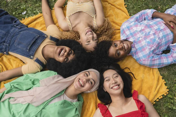Happy youth, multiethnic women having fun lying on the grass in the park - Concept of diversity and friendship young women -