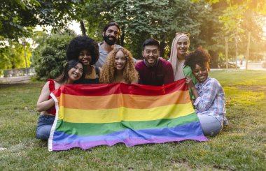 Genç çok ırklı insanlar parkta LGBT gökkuşağı bayrağı taşıyan bir grup fotoğrafı çekiyor.