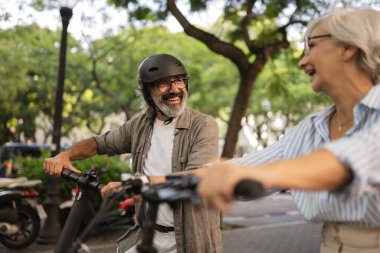 Mutlu son sınıf çifti şehirde motorsikletli ve elektrikli scooterlı gezinin tadını çıkarıyor. Her ikisi de gülümsüyor.