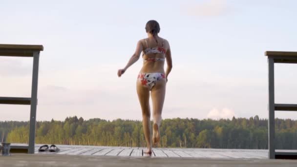 Ahşap iskeleden göle atlayan kadın. Yaz günü eğleniyorum. Rıhtımdan suya atlayan genç kız. — Stok video