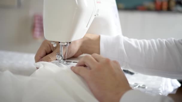 Mannen syr vid en symaskin. Designer sitter och syr. Dressmaker som arbetar med symaskinen. Begreppet konfektionstillverkning — Stockvideo