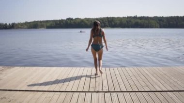 Ahşap iskeleden göle atlayan kadın. Yaz günü eğleniyorum. Rıhtımdan suya atlayan genç kız.