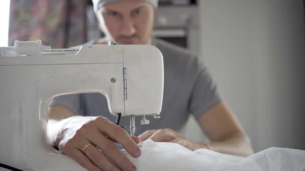De man naait aan een naaimachine. Ontwerper zit en naait. Kleermaker werkt aan de naaimachine. Concept van de kledingproductie — Stockvideo