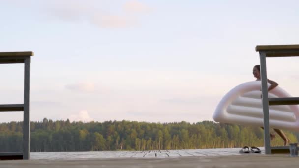 ティーネージャーは木製の桟橋の湖で空気マットレスで走る。夏の日に楽しんでいる女の子 — ストック動画