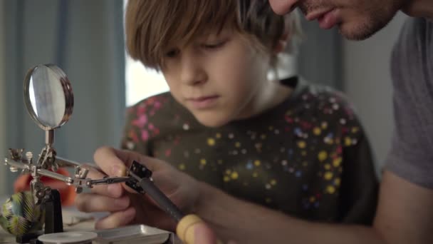 Babası küçük oğluna evde elektronik lensleri lehimlemeyi öğretiyor.. — Stok video