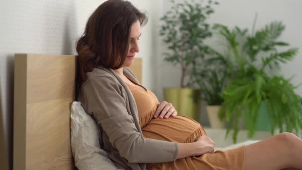 Une jolie femme enceinte s'assoit au lit. Le concept d'une grossesse heureuse. 9 mois d'attente pour un bébé. — Video