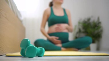 Arka planda hamile bir kadın var. Dambıllardaki ön plana odaklan. Spor konsepti.