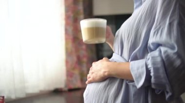Sevimli hamile kadın elinde bir fincan kahve tutuyor. Mutlu hamilelik kavramı. Sağlıklı içki değil