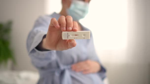 Mujer embarazada haciendo la prueba. Primer plano de los dedos que sostienen la prueba de covidio de antígeno expreso, resultado positivo — Vídeo de stock
