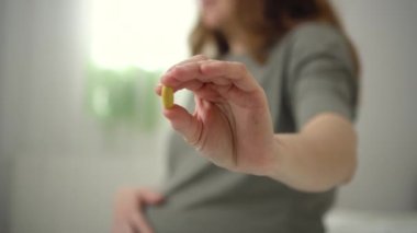Elimizdeki haplara yakından bak. Arka planda hamile bir kadın var. Hamilelik sırasında vitamin almak