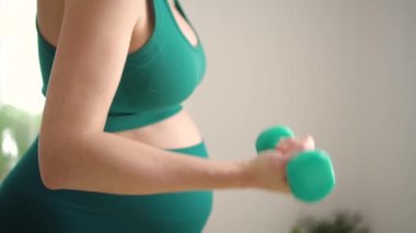 Hamile kadın dambıllarıyla egzersiz yapıyor. Hamilelik boyunca sağlıklı bir yaşam tarzı. Spor aktiviteleri