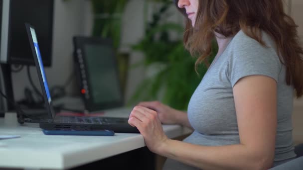 En gravid kvinna jobbar på en bärbar dator. Arbete under graviditeten hemifrån. — Stockvideo