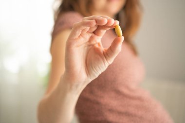 Elimizdeki haplara yakından bak. Arka planda hamile bir kadın var. Hamilelik sırasında vitamin almak