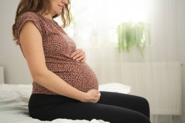 Sevimli hamile bir kadın yatakta oturur. Mutlu hamilelik kavramı. Bir bebek için 9 ay bekledim..