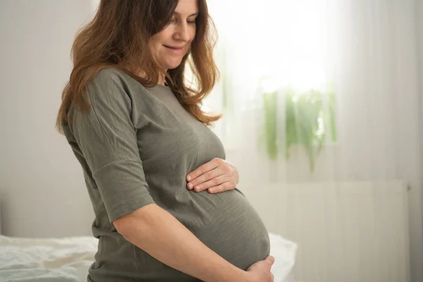 Seorang wanita hamil lucu duduk di tempat tidur. Konsep kehamilan yang bahagia. 9 bulan menunggu seorang bayi. — Stok Foto