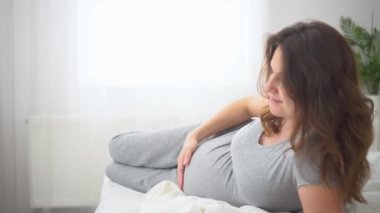 Sevimli hamile bir kadın yatakta oturur. Mutlu hamilelik kavramı. Bir bebek için 9 ay bekledim..