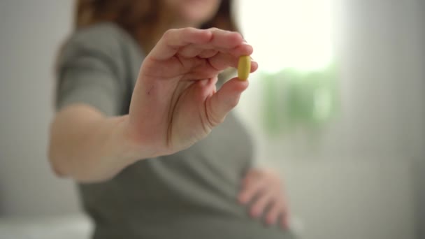 Крупный план таблеток в руке. На заднем плане беременная женщина. Принимать витамины во время беременности — стоковое видео