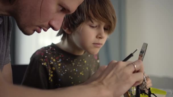 Отец учит своего маленького сына паять электронные контакты дома. — стоковое видео