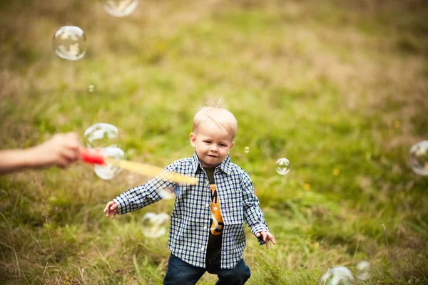 Baby boy on green grass outdoor playing with soap bubbles — Stock Photo, Image