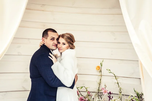 Bruiloft. pasgetrouwden omarmen tegen de achtergrond van prachtige bloemen en gordijnen — Stockfoto