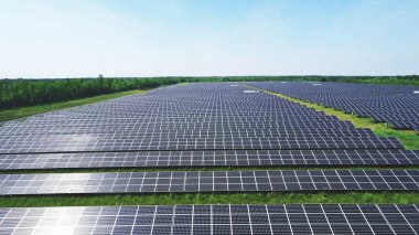 beautiful aerial view of solar panels on solar farm during a sunny day with plants and sky in the background. clipart