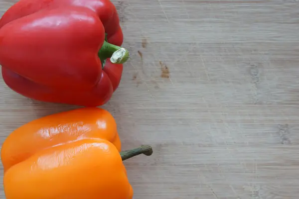 Un pimiento rojo y naranja en una tabla de cortar de madera — Foto de Stock