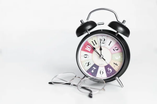 Reloj despertador negro sobre fondo blanco. Las gafas se encuentran al lado del reloj — Foto de Stock