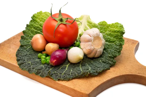 Чеснок, лук, горох, помидоры, листья капусты на кухонной доске — стоковое фото