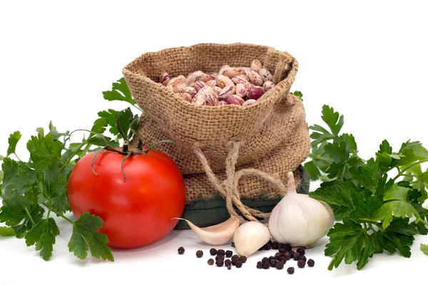 Fagioli in un sacchetto circondato da pomodoro, aglio, pepe e prezzemolo isolato — Foto Stock