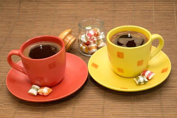 Yellow and orange cup of coffee with colorful candies and glass bowl between them — Stock Photo, Image