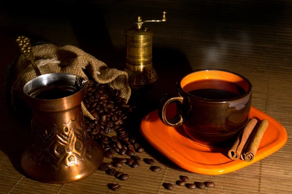Kávová zrna se vylila z vaku, mlýnek na kávu, kávové konvice, šálek kávy a skořice — Stock fotografie