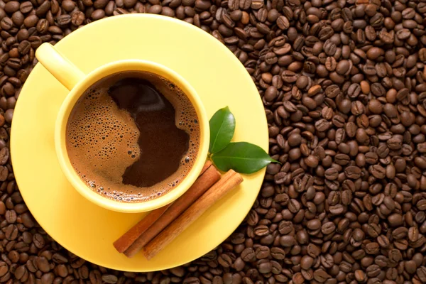 Gele kopje koffie met kaneel en groene bladeren — Stockfoto
