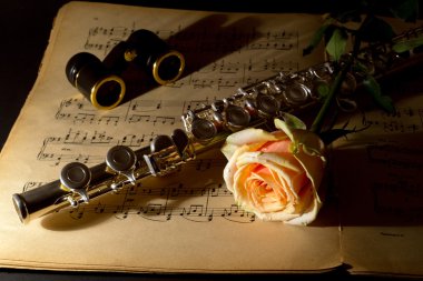 Opera glasses, silver flute and yellow rose on an ancient music score clipart